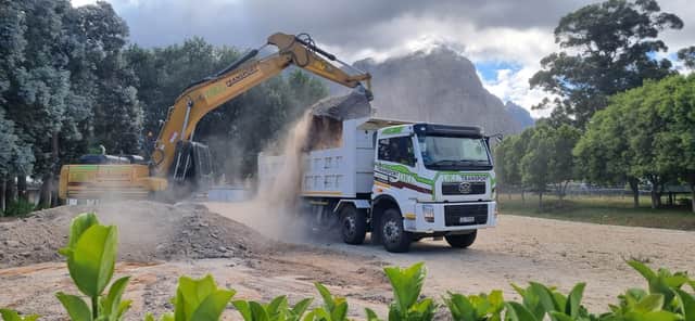 DKL excavator loading a FAW tipper truck with mountain backdrop