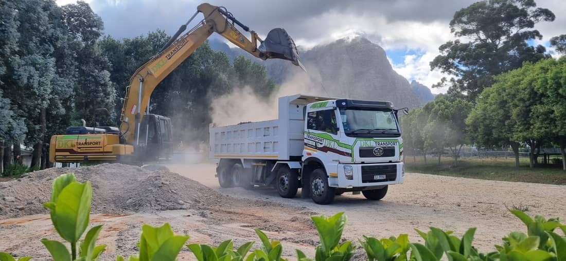 DKL excavator and tipper working on construction site with mountain backdrop